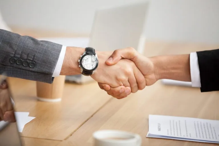 two business professionals shaking hands, symbolizing a coming to agreement on terms.